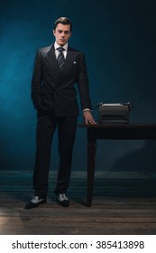 Vintage 1940s Business Man In Suit And Tie Standing Next To Desk With Typewriter.