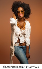 Vintage 70s Fashion Black Woman With Sunglasses. White Shirt And Jeans Against Brown Background.
