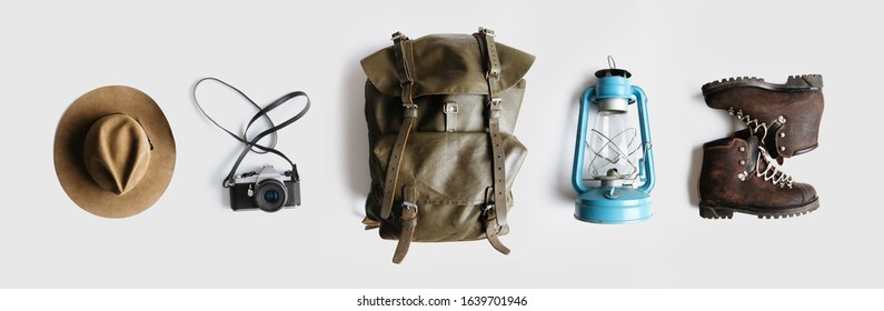 Vintage adventurer essential gear flat lay. Hat, backpack, film camera, gas lamp and boots on white background isolated. Minimal style hiking concept. Wanderlust vibes. - Shutterstock ID 1639701946