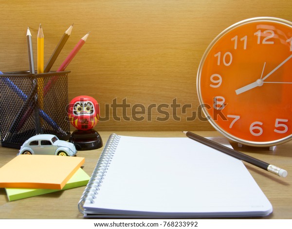 Vintage alarm clock, penciles, car toy,\
Post note paper sheet, Solar Doll on wooden\
floor