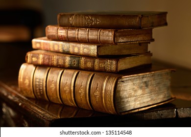 Vintage, antiquarian  books pile on wooden surface in warm directional light. Selective focus.
