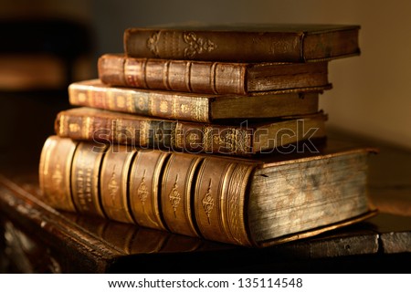 Vintage, antiquarian  books pile on wooden surface in warm directional light. Selective focus.