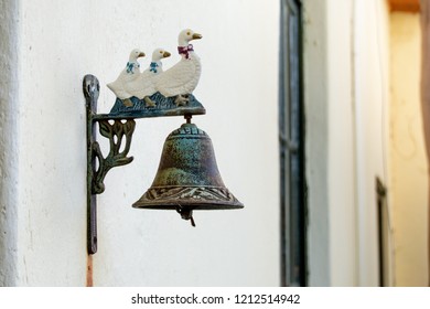 A vintage / antique door bell mounted on the wall of a traditional old farm house. It is styled with a row of ducks and has started to rust.