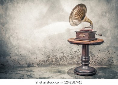 Vintage antique gramophone phonograph turntable with brass horn and red color vinyl disc record on wooden table front concrete wall background with shadow. Retro old style filtered photo - Shutterstock ID 1242587413