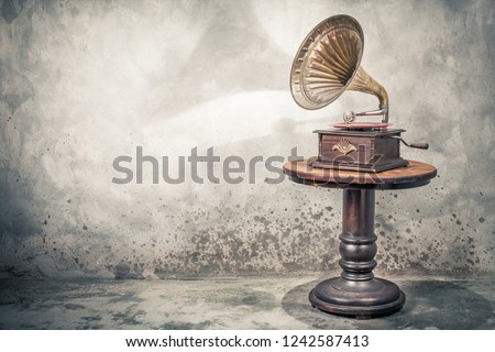 Vintage antique gramophone phonograph turntable with brass horn and red color vinyl disc record on wooden table front concrete wall background with shadow. Retro old style filtered photo
