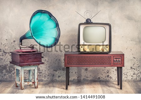 Vintage antique mint blue gramophone phonograph turntable on aged stool and old television from 50s on wooden TV stand front grunge textured loft concrete wall background. Retro style filtered photo