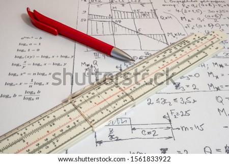 Vintage antique slide rule, logarithmic scale, calculations on paper,  and pen.