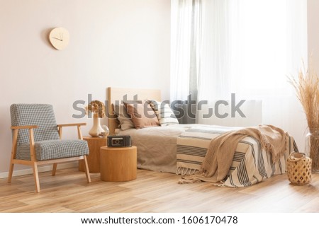 Vintage armchair next to wooden tables with retro camera and flowers on vase in elegant hotel room