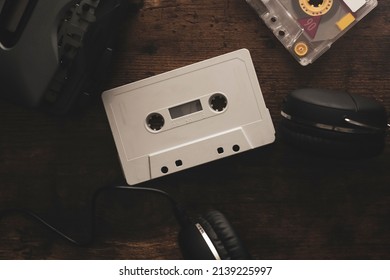 Vintage audio cassette between headphones and personal cassette player on a wood surface