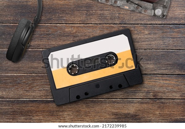 Vintage audio cassette between headphones and\
personal cassette player on a\
surface