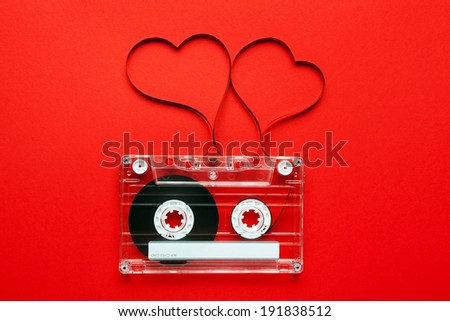 Vintage audio cassette with loose tape shaping two hearts on red background 