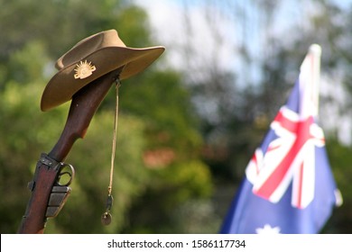 Vintage Australian Army 303 rifle, a soldier's dogtags, iconic Aussie slouch hat (clearly showing the rising sun badge) and a floral wreath with Australian National Flag in background on ANZAC Day.