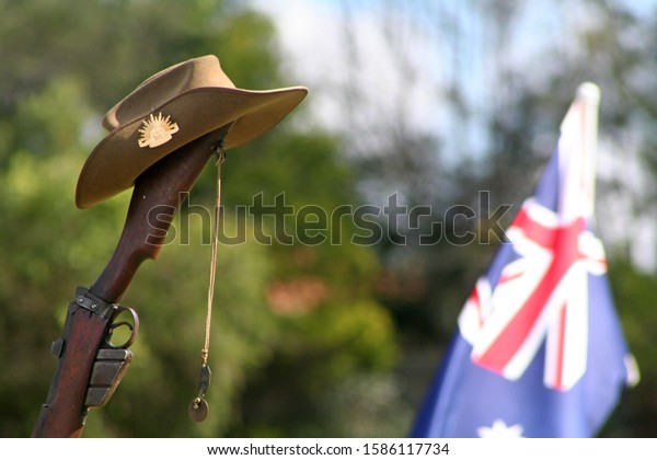 Vintage Australian Army 303 rifle, a soldier\'s\
dogtags, iconic Aussie slouch hat (clearly showing the rising sun\
badge) and a floral wreath with Australian National Flag in\
background on ANZAC\
Day.