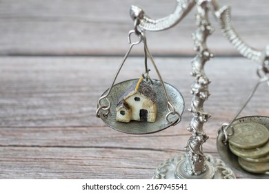 Vintage Balance Scale With Mini House And Old Coins On A Rustic Wood Table. The Concept Of Family Budget, Home Finances, Money Management, Saving, And Spending. A Close-up.