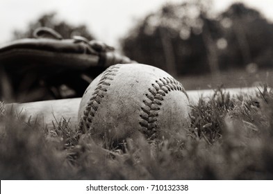 Vintage baseball laying on the field in horizontal view with equipment in the background.  Ball is old and used.