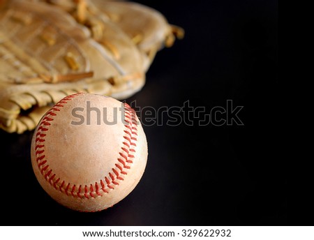 Vintage baseball mitt and old, dirty baseball with side lighting on black background.