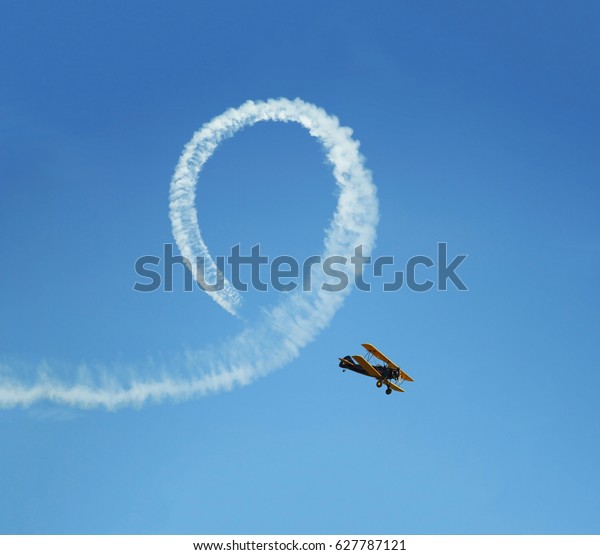 Vintage biplane\
does loop stunt with smoke\
trails