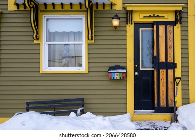 A vintage black door with yellow trim on a green wooden house. The door has a glass window with a wood shutter. Above the door are decorative decals and a light fixture. There's a small glass window. - Powered by Shutterstock