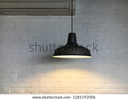 Vintage black fixture of light hang on ceiling in the room corner and have white bricks wall and a part of air conditioner background.
