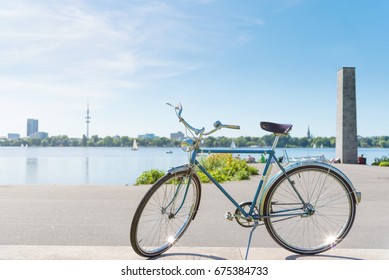 vintage blue bicycle parked at lakeshore of Alster Lake in Hamburg, Germany under beautiful clear blue summer sky with cityscape in blurred background - Powered by Shutterstock