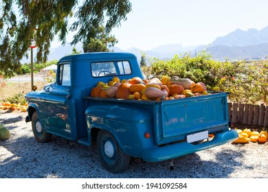 A vintage blue pickup truck loaded with colorful pumpkins. Misty mountains in the background.