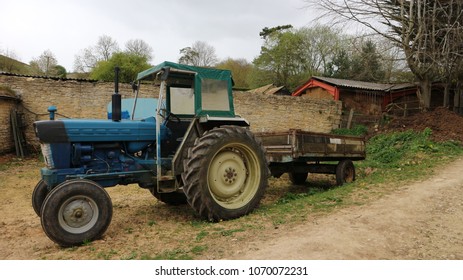 Vintage Blue Tractor With Trailer On Farm Yard