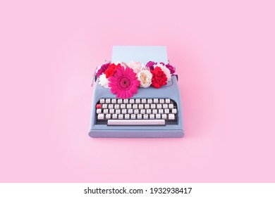 Vintage blue typewriter with colorful flowers on pastel pink background. Creative spring concept.