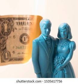 Vintage Blue Wedding Cake Topper Couple In Front Of A Dollar Bill On Fire. Weddings Can Be Costly And A Waste Of Money. Couple Fighting Over Finances. Man And Wife In Financial Trouble Or Divorce.