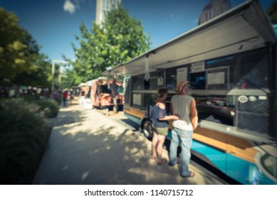 Vintage Blurred Food Truck Vendor Customers Buy And Taste Variety Of Foods. People Waiting, Queuing In Line To Pick Up Lunch And Drink Delivery At Urban Park In Dallas, Texas, USA, Blue Sky Wide View