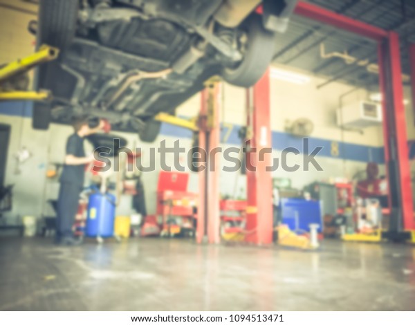 Vintage blurred mechanic changing oil below of\
lifted car at auto shop in Texas, USA. Defocused background\
interior of modern oil change service station. Working technician\
at garage concept