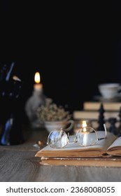 Vintage books, reading glasses, gold pen, hand model, gold jewelry, scented candles, flowers, chess pieces and cup of tea or coffee on the table. Dark academia concept. Selective focus.