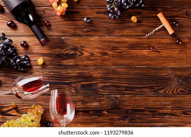 Vintage bottle of red wine with blank matte black label, corkscrew & bunches grapes on wooden table background. Expensive bottle of cabernet sauvignon concept. Copy space, top view, flat lay.