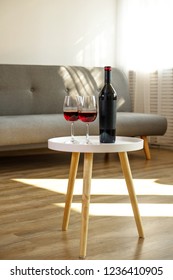 Vintage Bottle Of Red Wine With Blank Matte Black Label On Table With Two Glasses In Empty Loft Living Room. Expensive Bottle Of Cabernet Sauvignon Concept. Copy Space, Top View, Close Up.