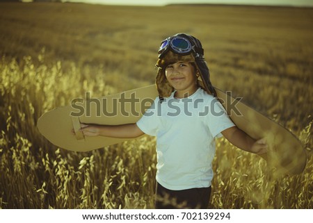 Vintage, Boy playing to be airplane pilot, funny guy with aviator cap and glasses, carries wings made of brown cardboard as an airplane
