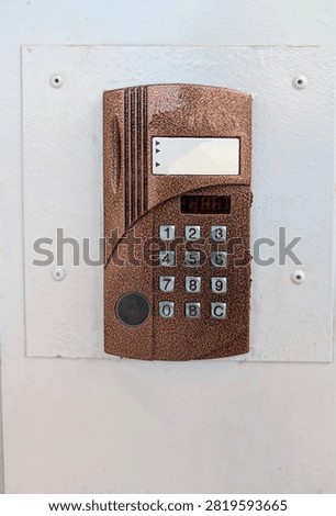 A vintage brown intercom device with buttons is mounted on a white wall. Building security access control and residential entryway door communication system.