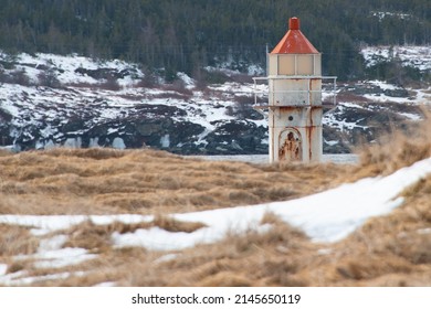 A Vintage Caisson Style Tower With A Round Red Metal Roof.  In The Center Of The Lighthouse Is A Vintage Lamp Made Of Multiple Pieces Of Glass. A Catwalk Made Of Metal Is Around The Beacon.