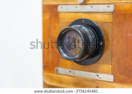 Vintage camera against light background, large lens with multiple rings, dark body possibly black or dark brown, metal components, film advance knob, matte finish, no text or branding, even lightin