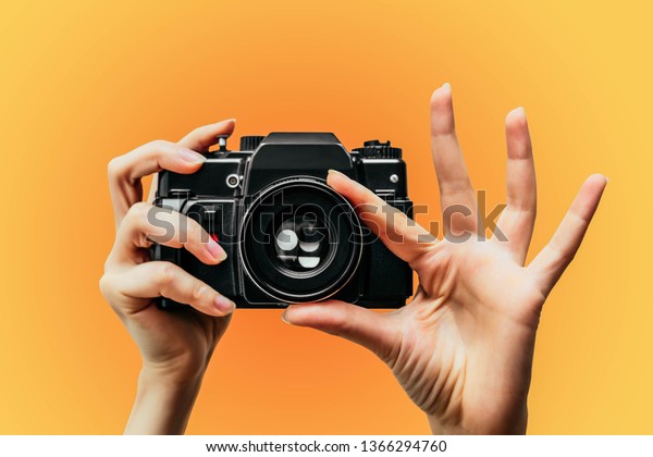 Vintage Camera in female hand. A\
photo. Photographer. Manual focus. Colored background.\
orange