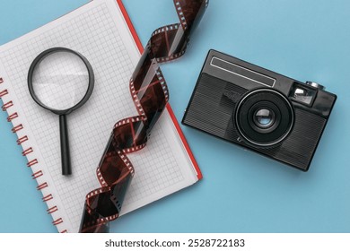 Vintage Camera and Film with Notebook and Magnifying Glass on Blue Background - Powered by Shutterstock