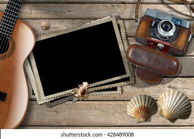 Vintage Camera With Leather Case, Acoustic Guitar, A Group Of Empty Photos Frames And Seashells On A Wooden Boardwalk With Sand