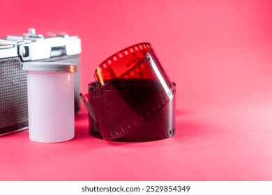 A vintage camera with a roll of film and a film canister on a bright pink background. The camera is metallic with a classic design, and the film is partially unrolled, showcasing its perforated edges. - Powered by Shutterstock