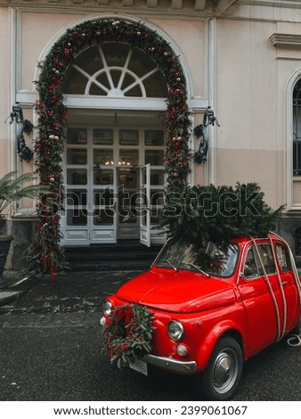 Vintage car with Christmas tree on top. Red Fiat vintage in Italy with New Year decoration in front of the building decorated Christmas style. Red car with Christmas tree on top