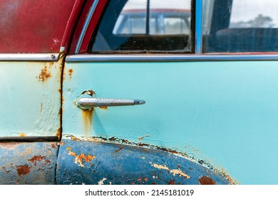 Vintage car door with rust and cracked faded paint around the handle