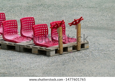Vintage children bus game from recycled materials, rough wood pallets and red plastic chairs, isolated on concrete background with nobody.