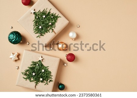 Vintage Christmas card design with craft paper gift boxes with Christmas trees and colorful Xmas balls on beige background. Flat lay. Top view.