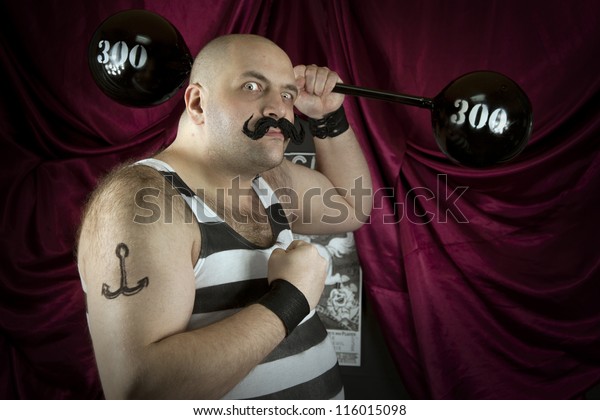 Vintage circus\
strongman holding big 300 lbs weights. Bald strong man in striped\
t- shirt lifting heavy weights. Vintage cinema circus scene. Part\
of larger vintage\
collection.