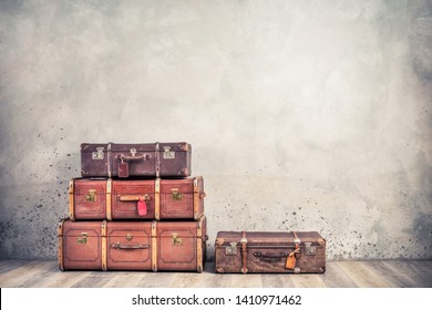 Vintage classic outdated trunks luggage with tags, old antique leather suitcases front textured aged concrete wall background. Travel baggage concept. Retro style filtered photo