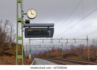 Vintage Clock And Black Board Of Train Schedule At Local  Bijorkliden Train Station In Late Summer With Background Of Train Track And Train Transmission Line, Abisko, Kiruna, Sweden