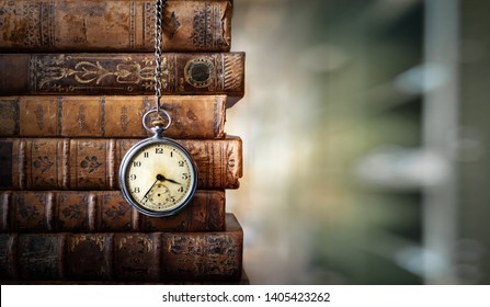 Vintage clock hanging on a chain on the background of old books. Old watch as a symbol of passing time. Concept on the theme of history, nostalgia, old age. Retro style. - Shutterstock ID 1405423262