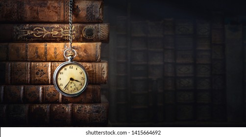 Винтажные часы, висящие на цепочке на фоне старых книг. Старые часы как символ уходящего времени. Концепция на тему истории, ностальгии, старости. Ретро-стиль.